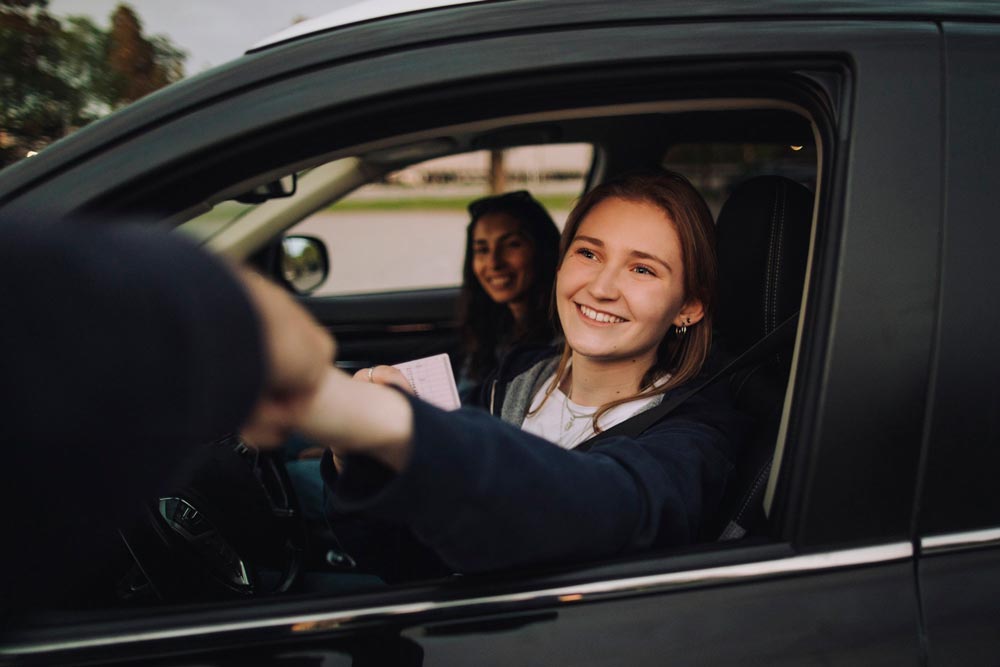 Leende ung kvinna ger knytnävsdunk och håller körkort i bilen med instruktör i bakgrunden